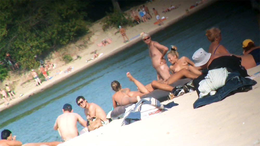 Two Nudists Posing Together on a Busy Riverbank