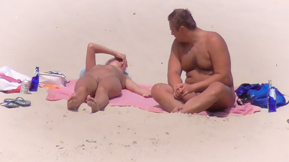 Opalování tváří dolů na růžové osušce na nudistické pláži