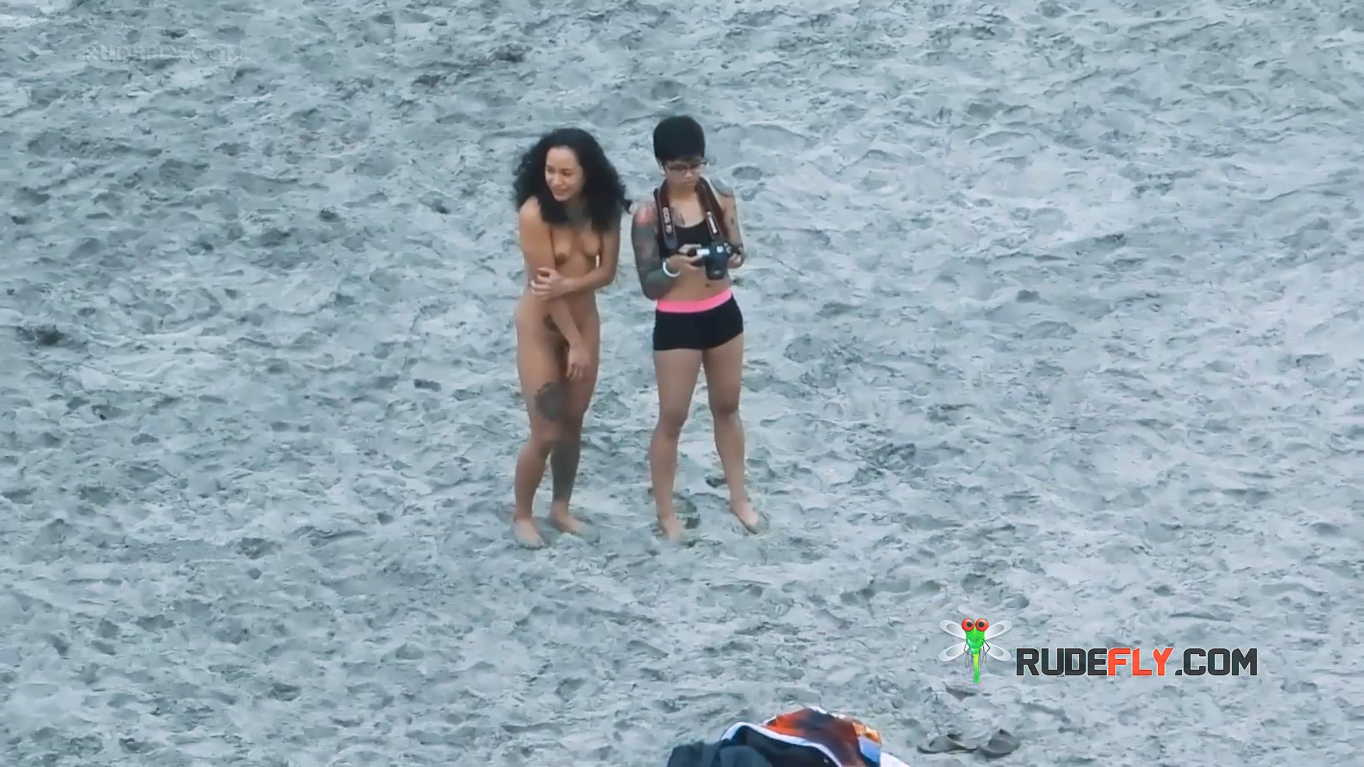 Two Naturists on the Sand with a Camera