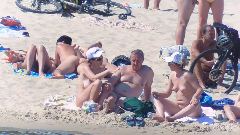 Four Nudists Gathered on the Beach Beside a Green Bag