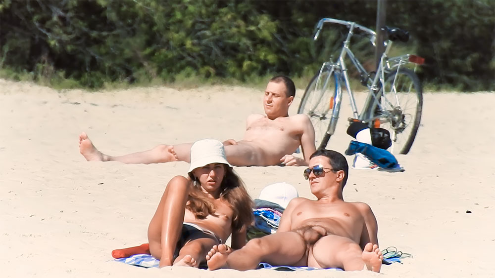 Three Nudists Sharing a Towel Spot Near a Bicycle