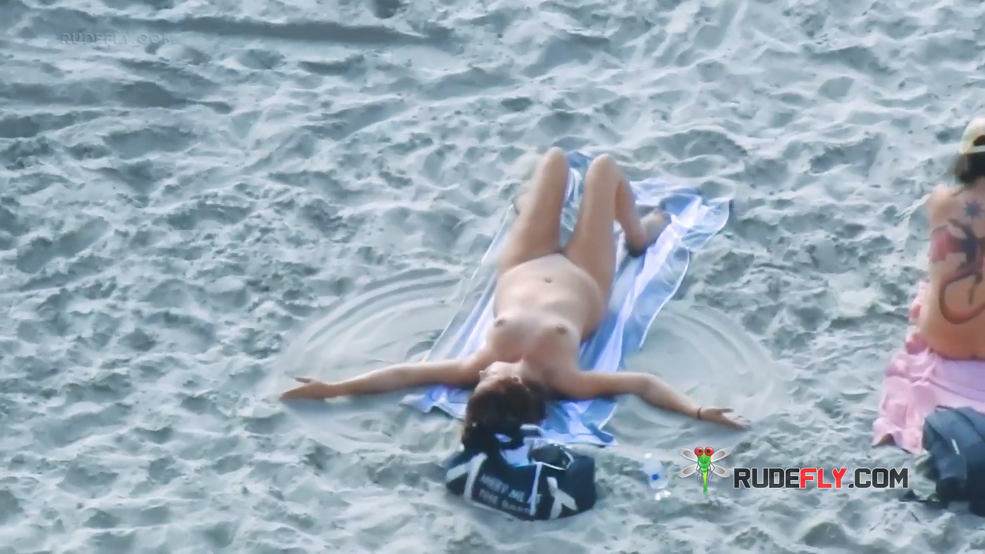 Pruhovaný ručník a taška na nudistické pláži