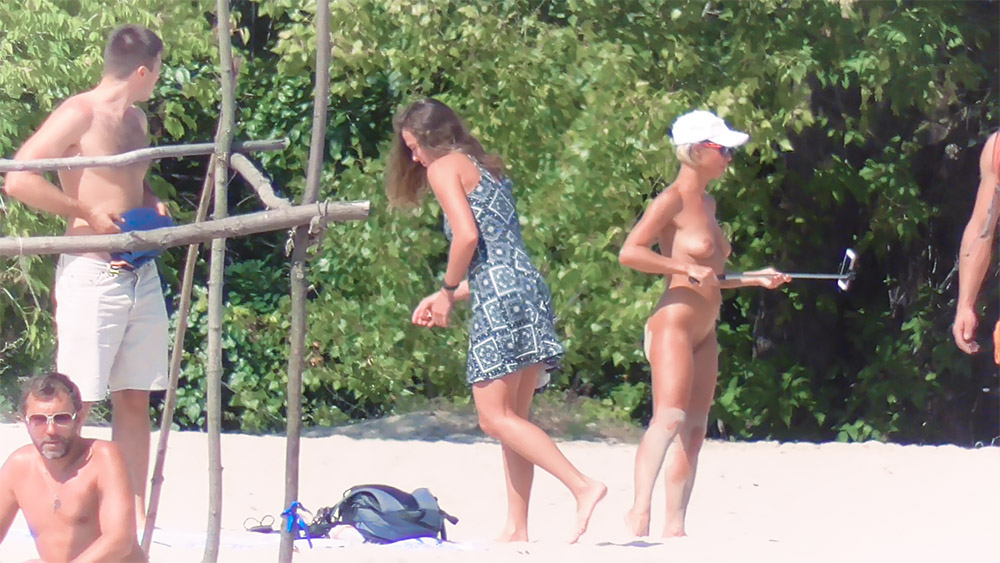 Čtyři naturisté na písku poblíž husté zeleně