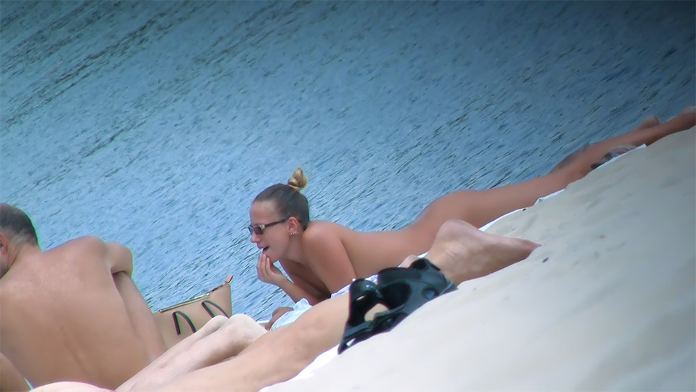 Three Nudists Resting Side by Side Near Calm Water