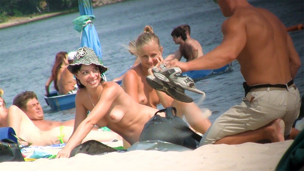 Twee vrouwen topless op het strand bij een blauwe parasol