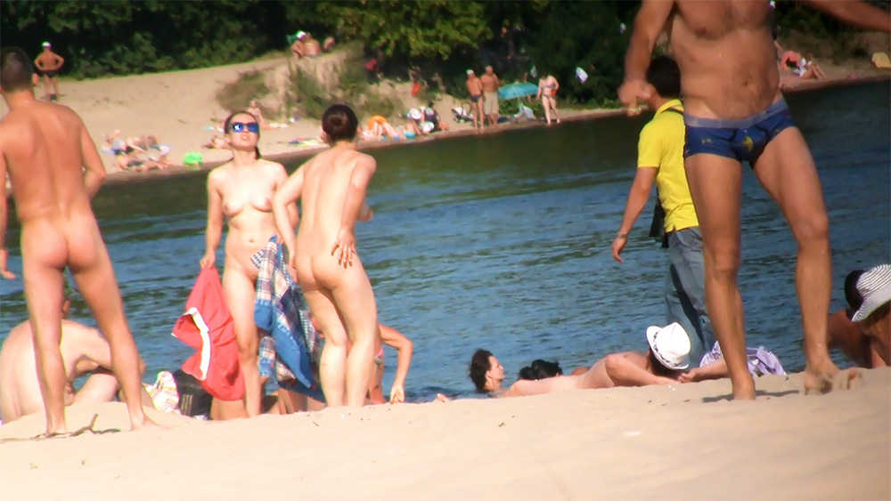 Two Nudists Pausing by the Shore with a Blue Towel