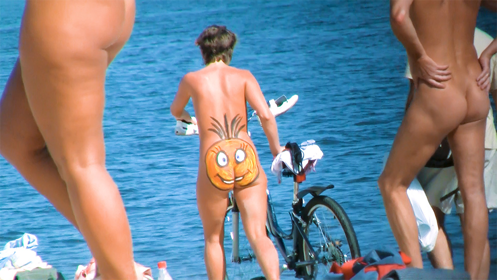 Žena na nudistické pláži s usměvavou malbou na těle a kolem