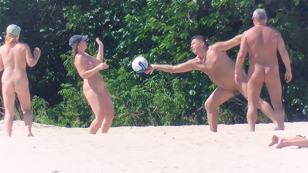 Tři hráči na nudistické pláži si přihrávají volejbalový míč