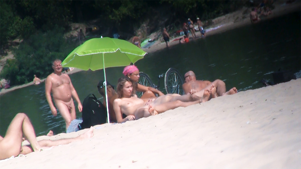 Five Nudists Gathered Beside a Calm Riverbank