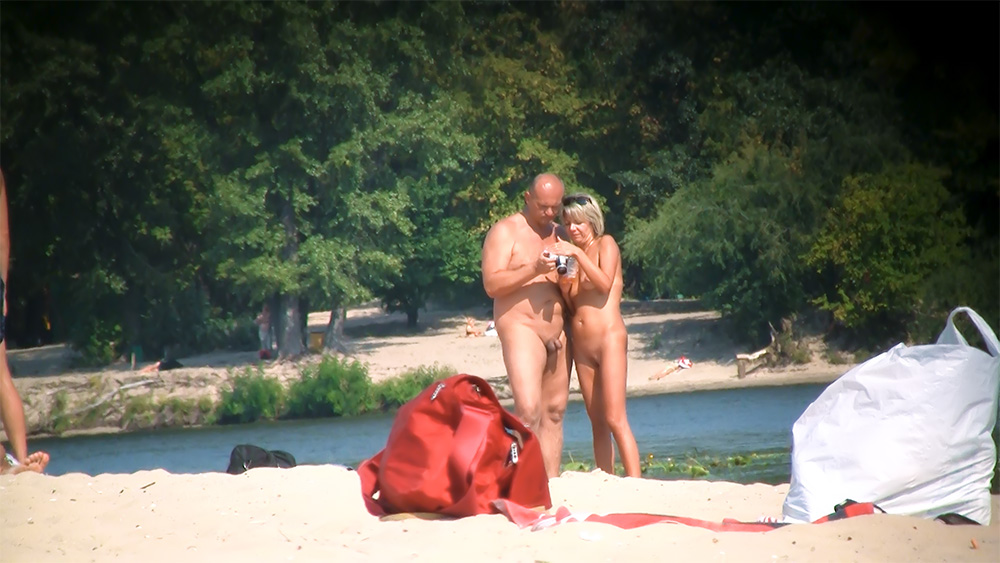 Dva nudisté kontrolují záběry na fotoaparátu u břehu řeky