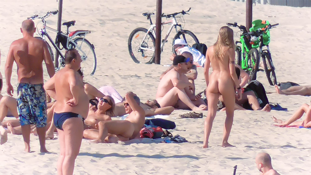 Standing Among Seated Nudists on a Sandy Beach