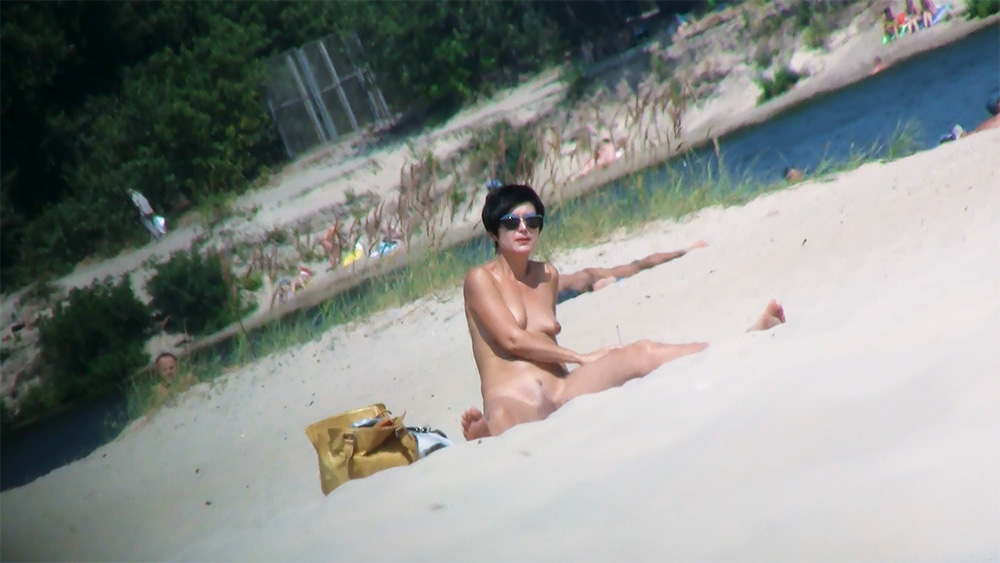 Žena pózuje na písku nudistické pláže