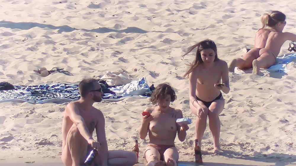 Tři návštěvníci pláže odpočívající na písku na topless pláži