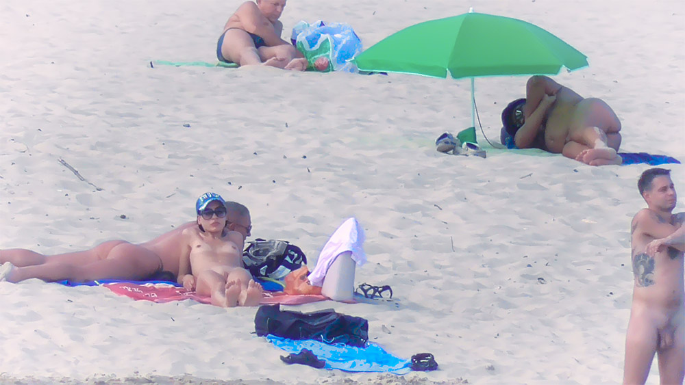 Tres nudistas relajándose juntos en una playa nudista de arena