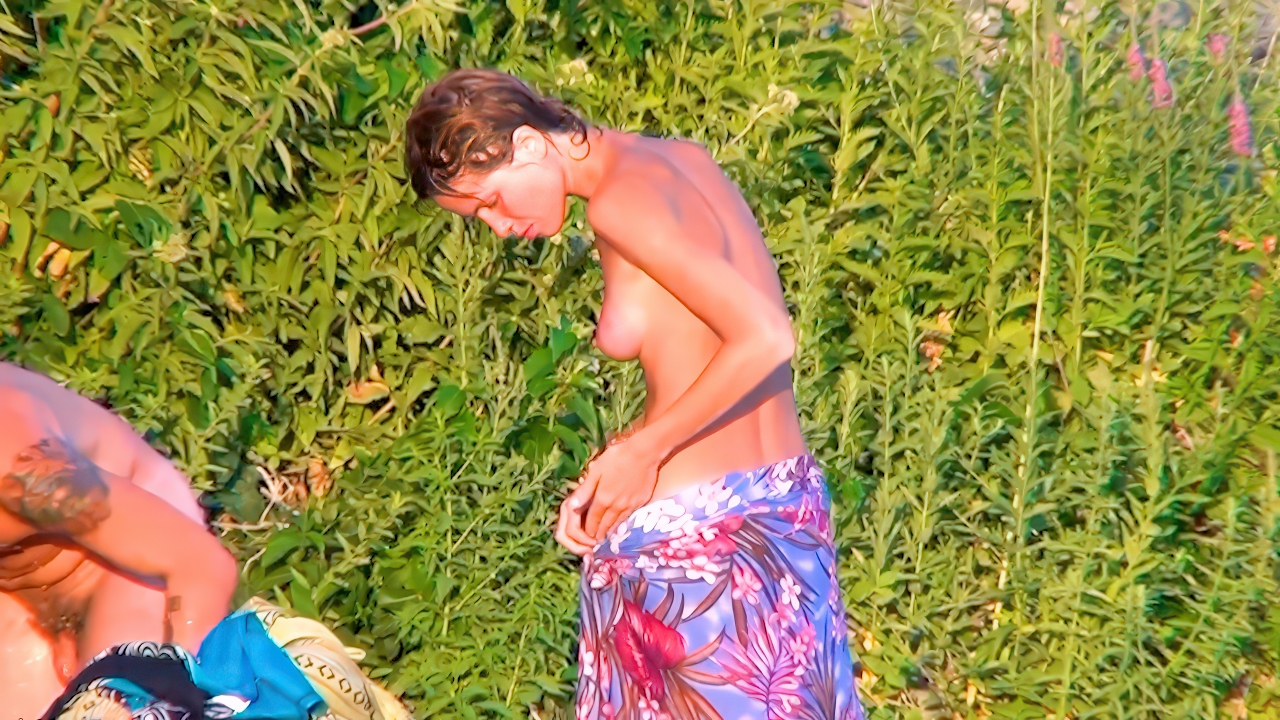 Among lush greenery, a topless woman and shirtless man relax on towels