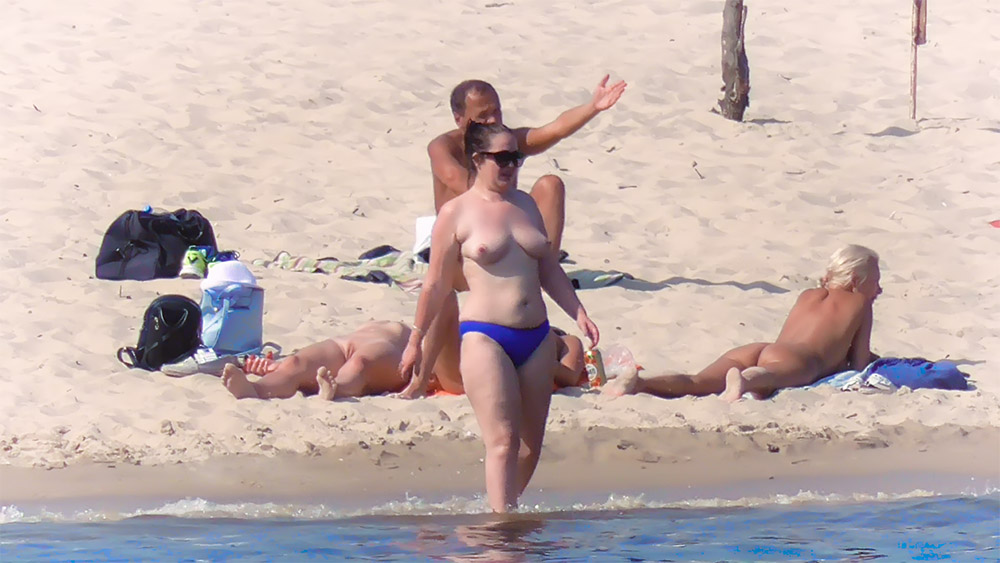 Topless vrouw in blauw bikinibroekje die het zand op stapt