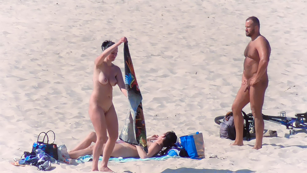 Two Nudists Setting Up a Towel on Sandy Shore