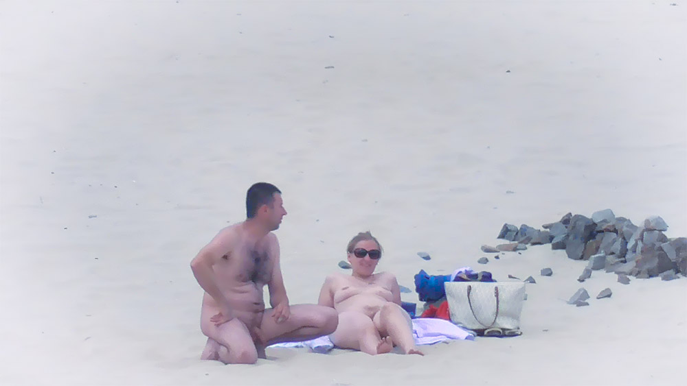 Naaktstrandkoppel naast een strandtas op het zand