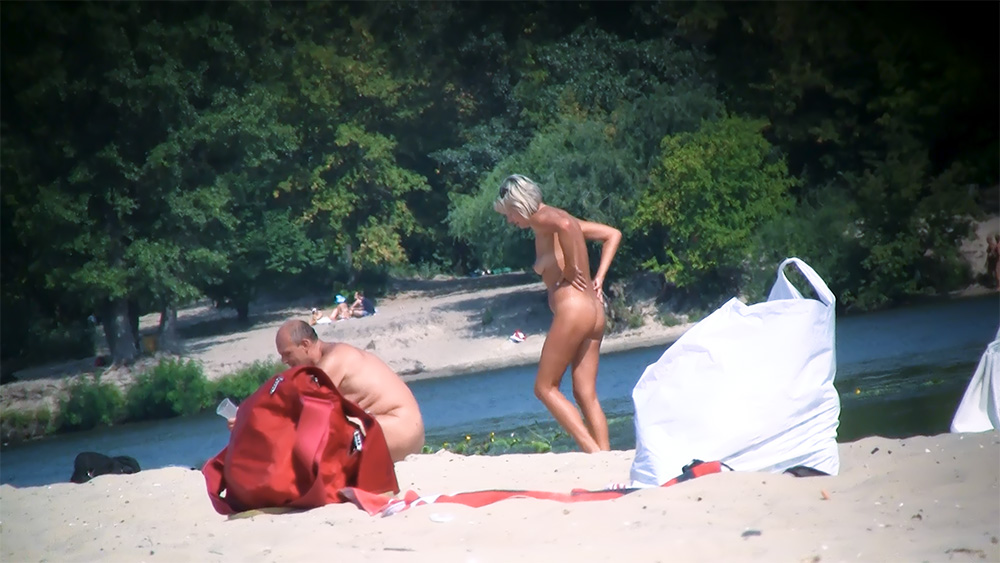 Nudists Standing and Chatting on a Sandy Riverbank Beach