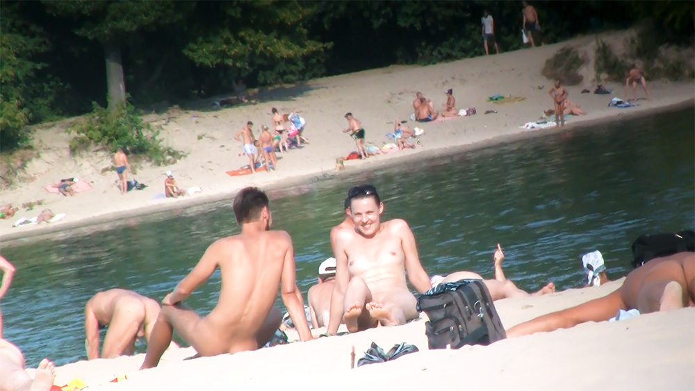 Three Naturists Resting Beside a Dark Backpack on the Shore