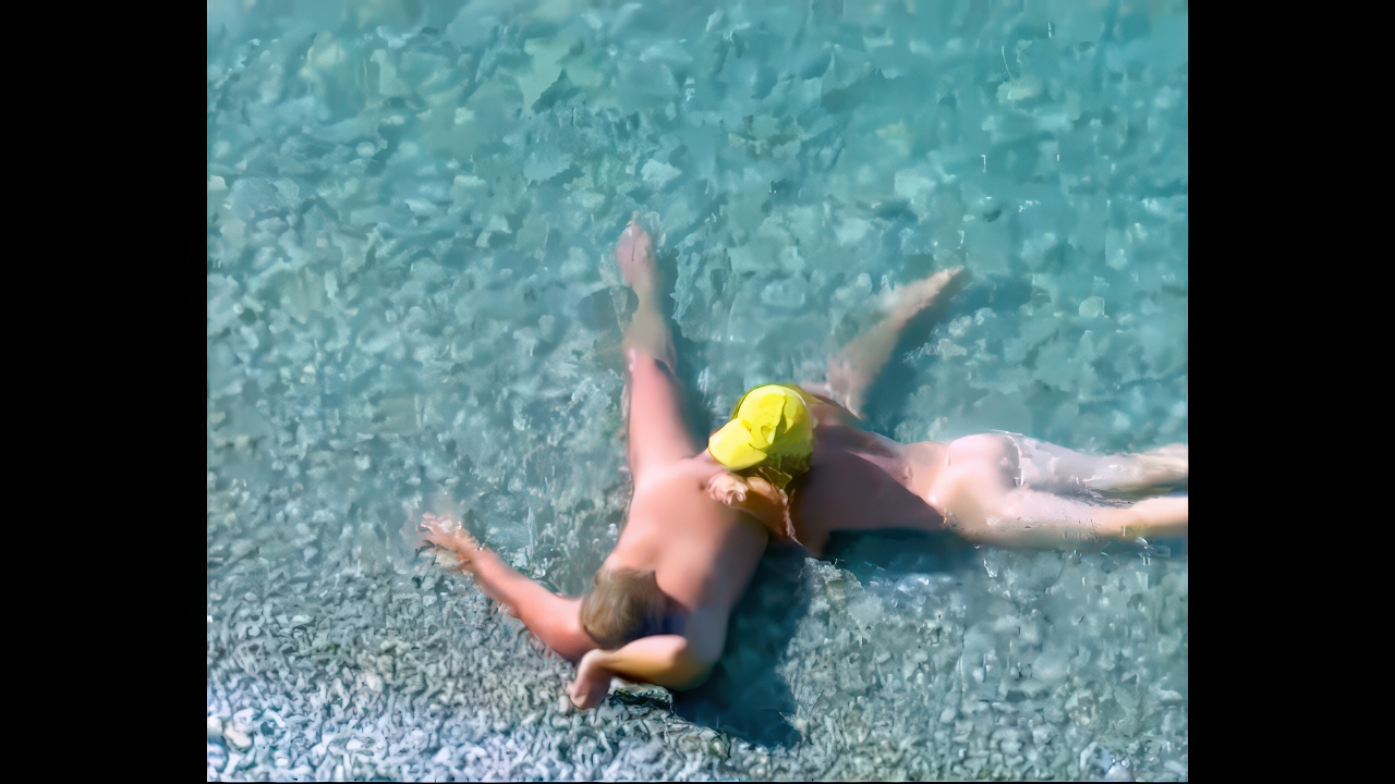 Spread-out nudist resting in bright shallow turquoise water