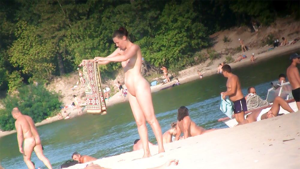 Unfolding a Patterned Towel on a Nude Beach Shore