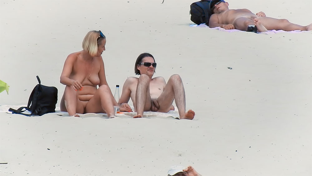 Two Nudists Resting on the Sand by the Shore