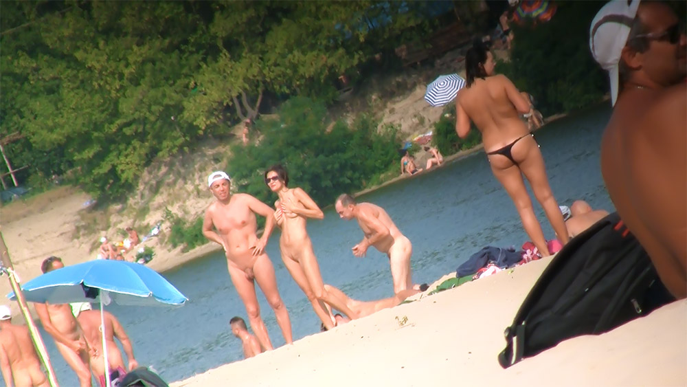 Tři nudisté stojí u vody na betonovém okraji
