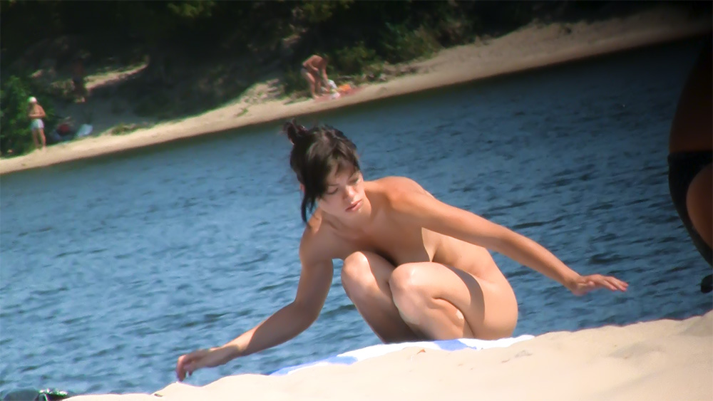 Nudistenvrouw balanceert op het zand bij het water