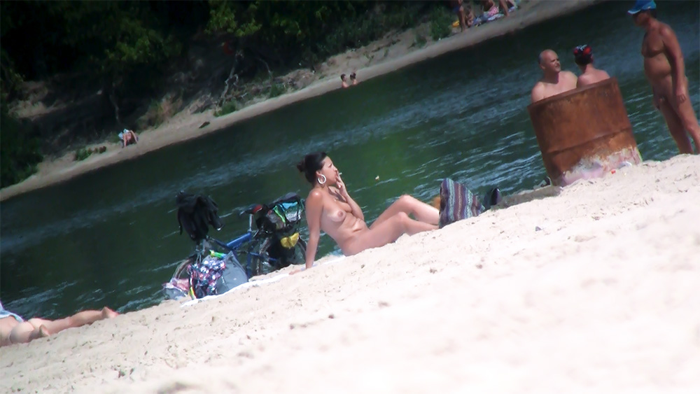 Opalující se žena na nudistické pláži kouří vedle zaparkovaného kola