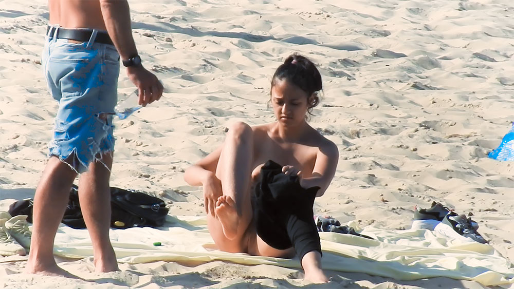 Attraper un vêtement sur une serviette de plage naturiste
