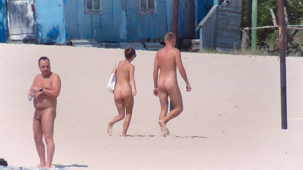 Pareja de playa nudista paseando junta por la arena abierta