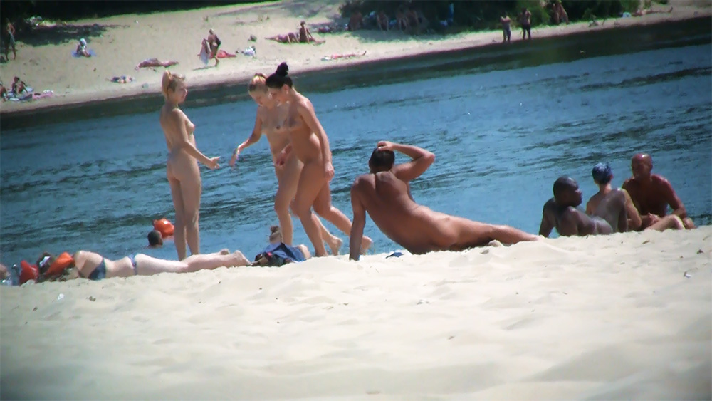 Six Naturists Gathered Along a Quiet River Beach