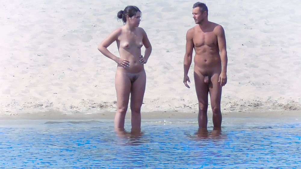 Písečné pobřeží nudistické pláže s povídajícím si párem
