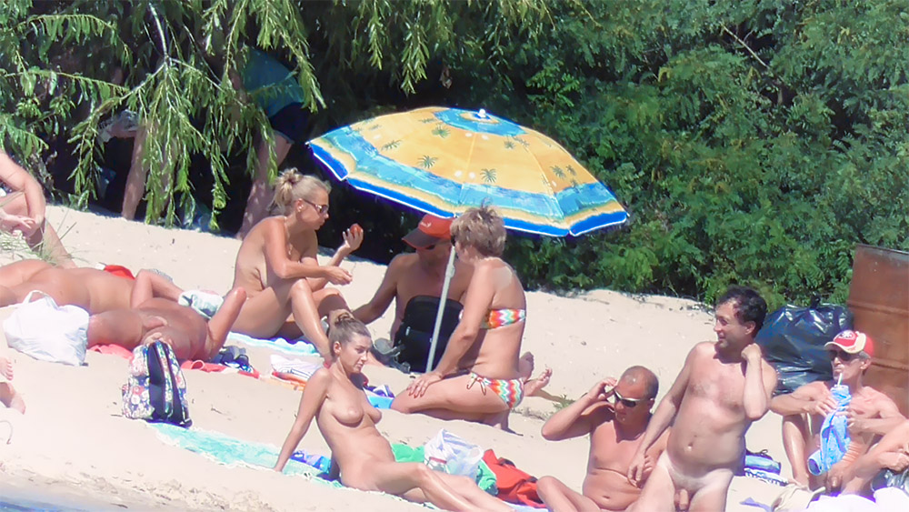 Five Naturists Gathered Around a Bright Beach Umbrella