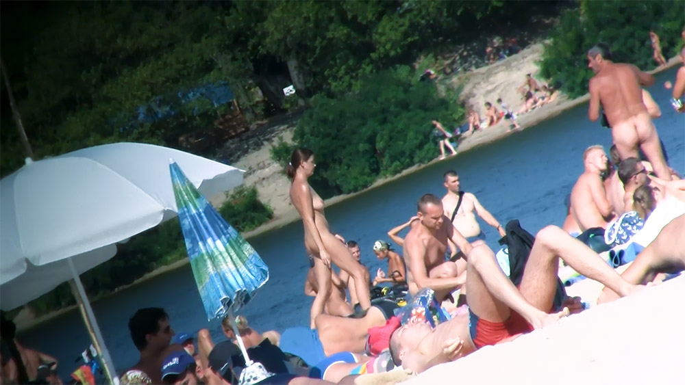 Rocky Riverbank Crowded with Naturists by the Water