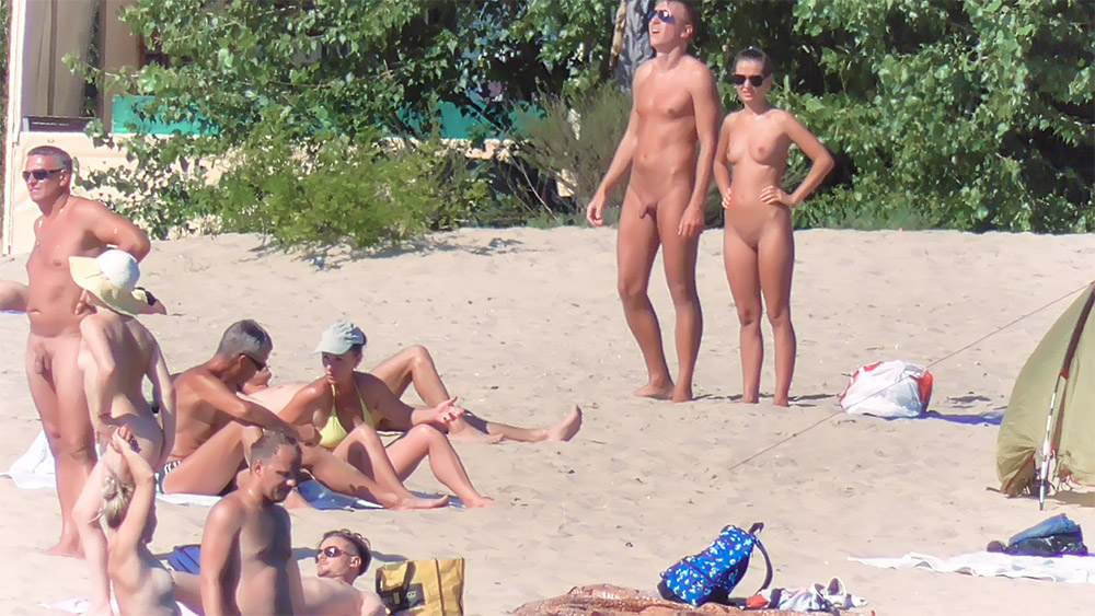 Due nudisti in posa su una ventilata spiaggia sabbiosa