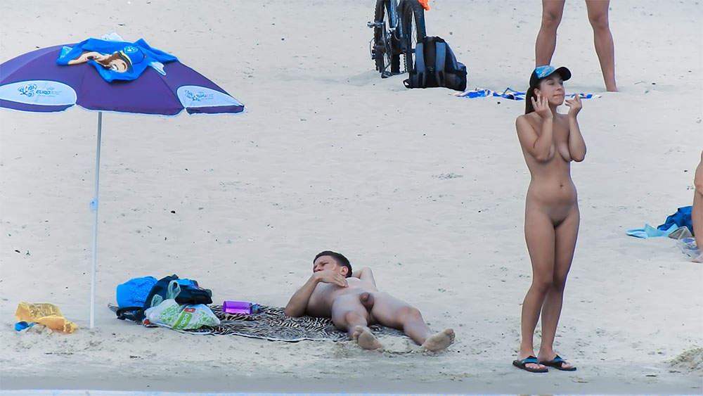 In piedi ad aggiustare un cappellino blu su una spiaggia nudista