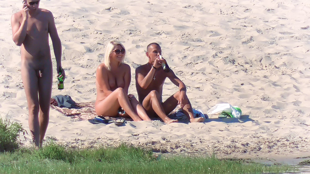 Pár na nudistické pláži sedící spolu na písku