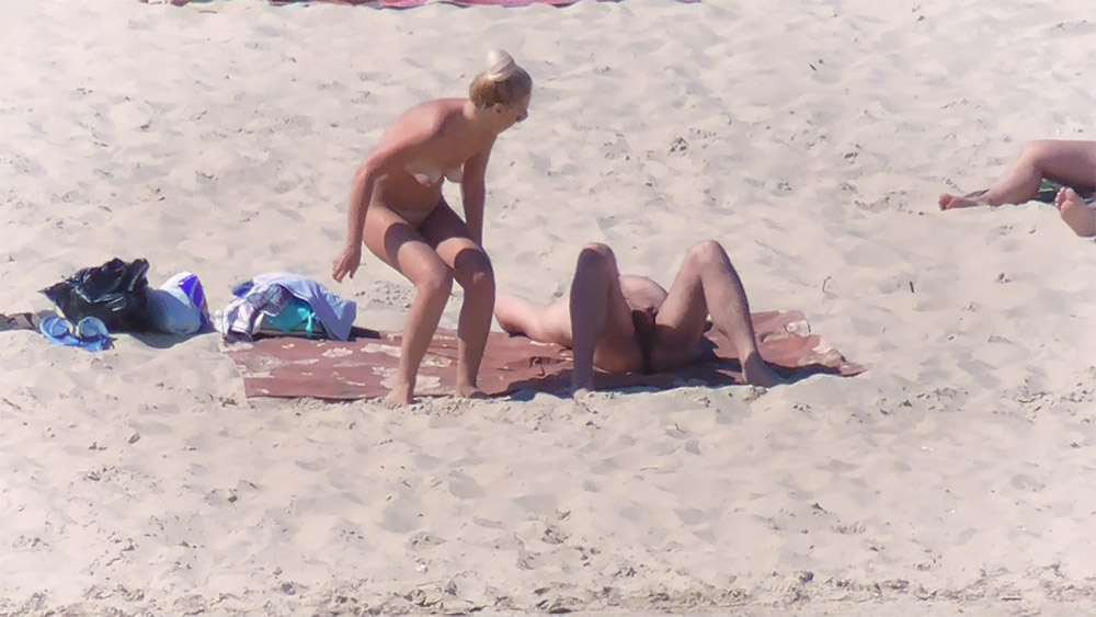 Two Nudists Sharing a Red Towel on the Sand
