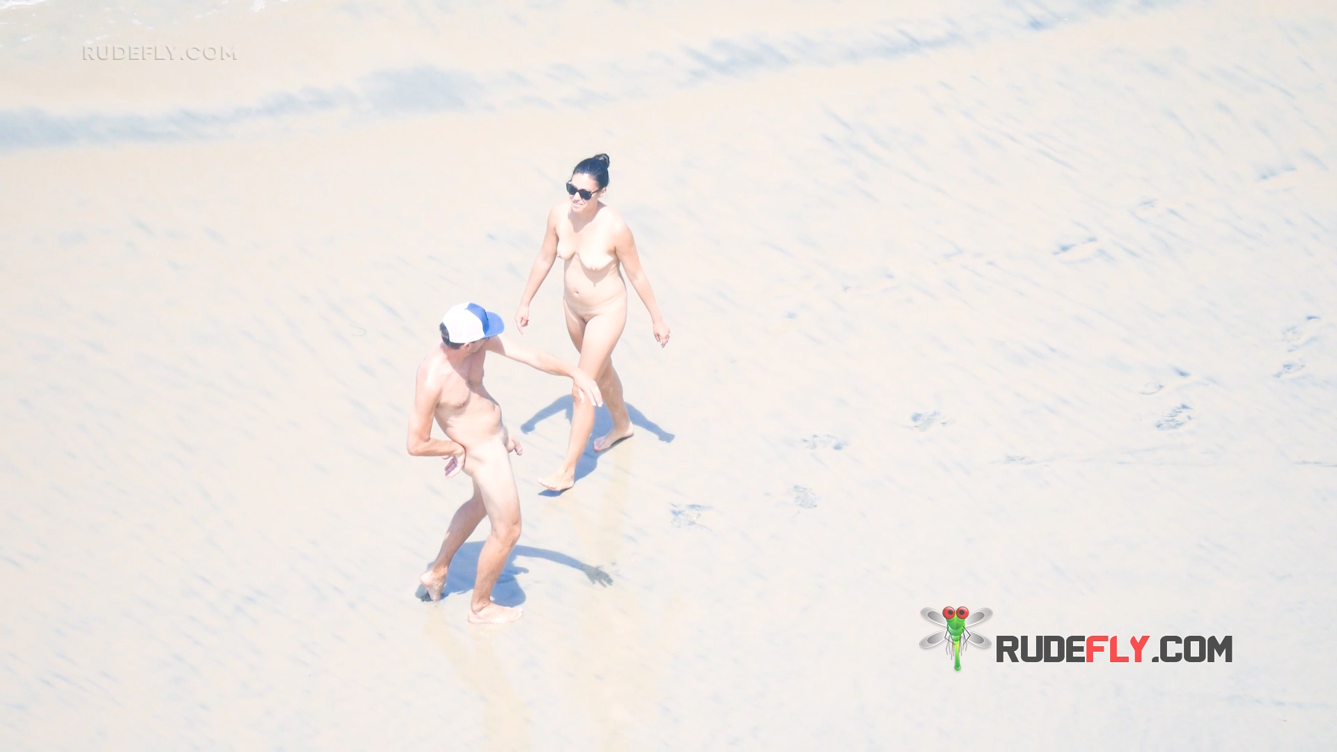 Two Nudists Strolling Across Sunlit Sand