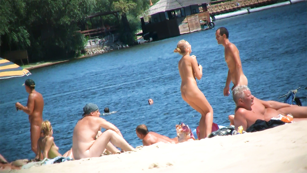 Five Naturists Gathered Near the Water with a Bicycle