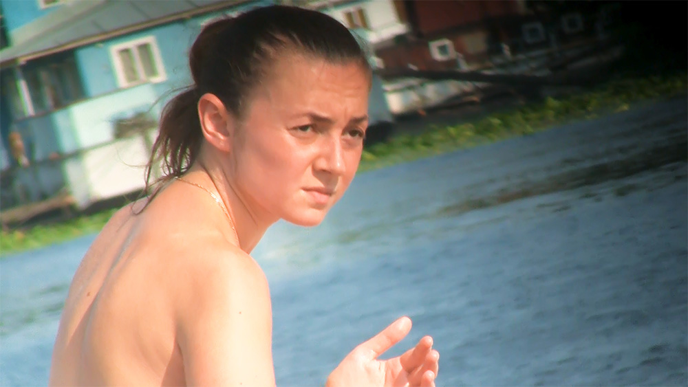 Nudistická pláž u jezera s tmavovlasou opalující se ženou