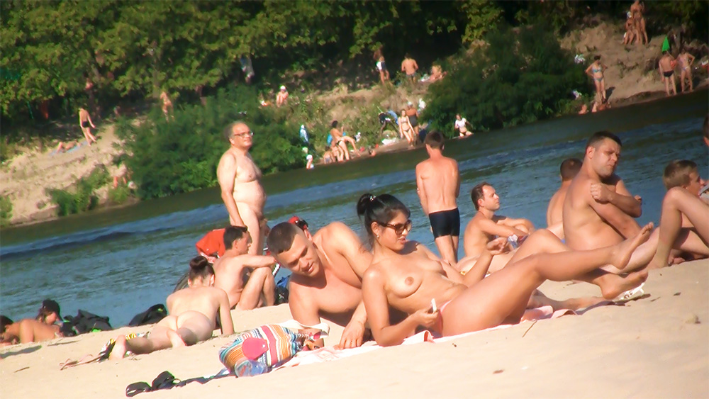 Nudisté odpočívající na písku blízko břehu
