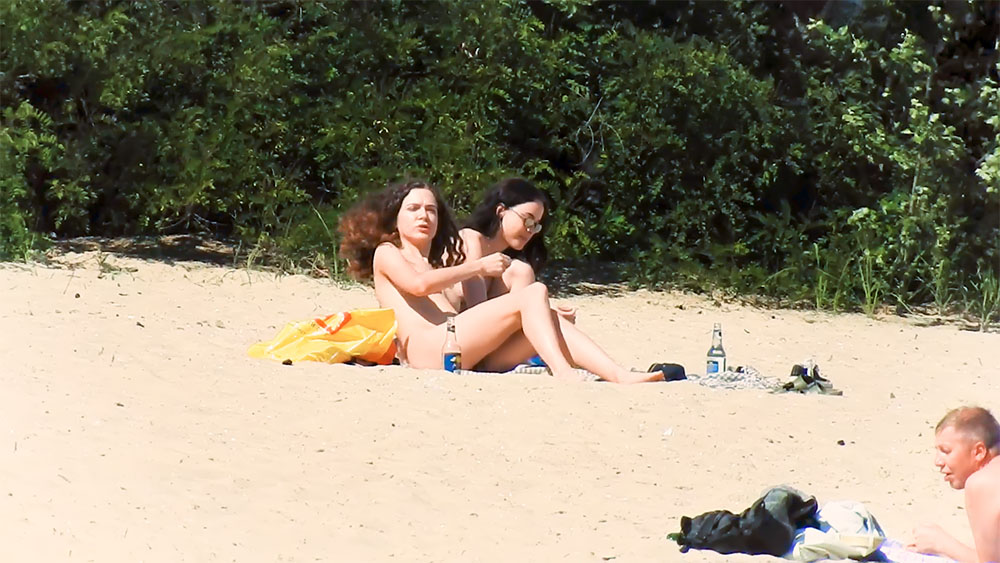 Due donne in topless sulla sabbia vicino alla linea degli alberi