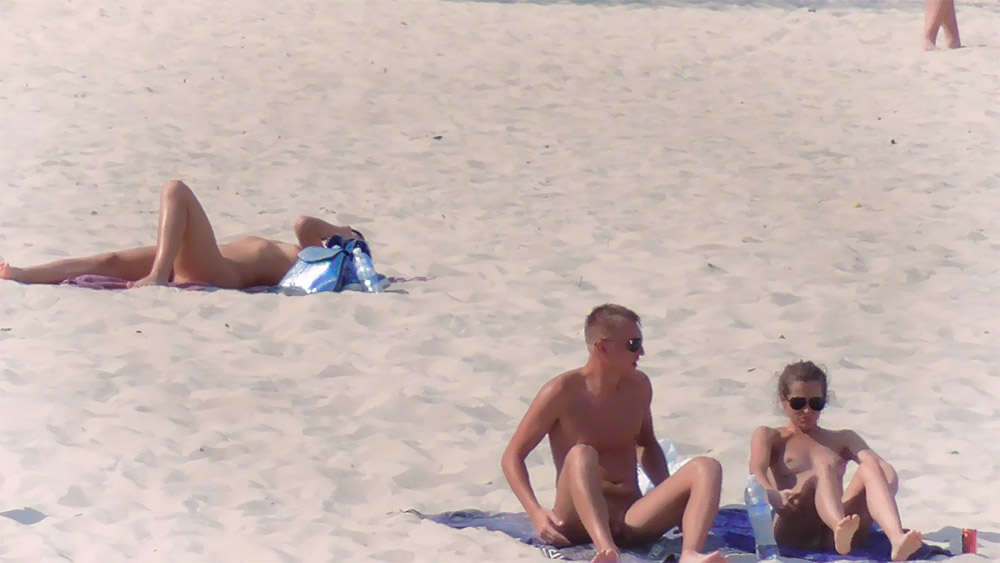 Two Nudists Resting on a Beach Towel in Sunglasses