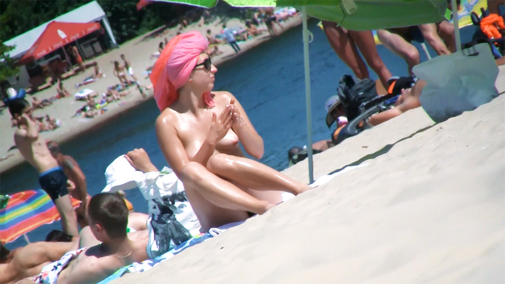 Nudist Applying Sunscreen on a Concrete Waterfront Ledge