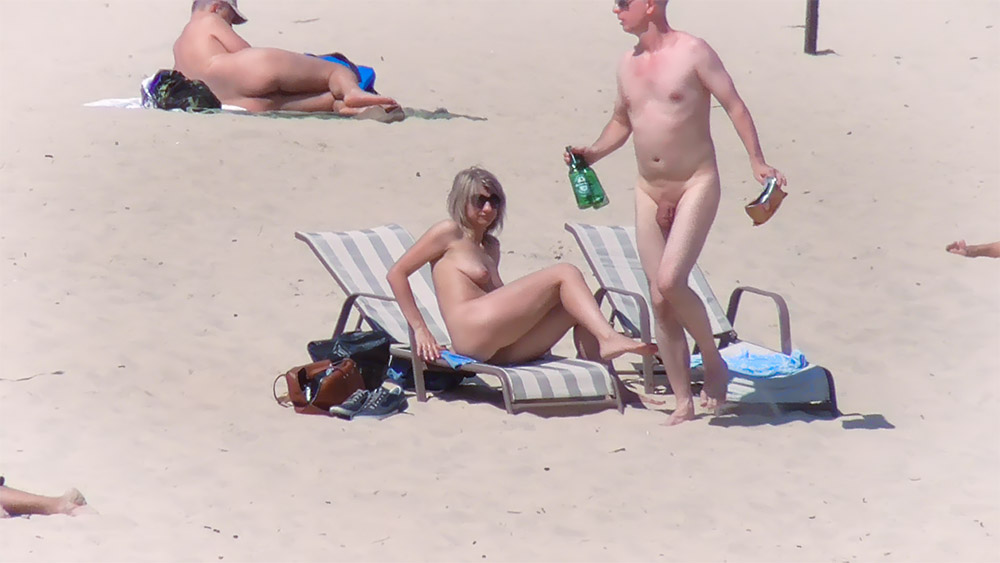 Dva nudisté si dopřávají nápoj na plážových lehátkách