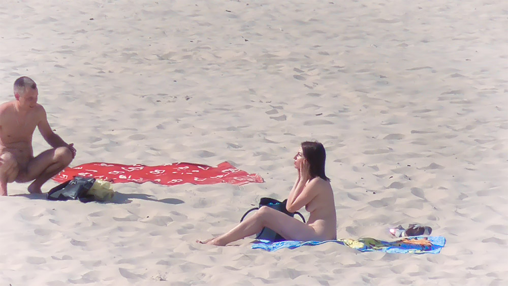 Sezení a stání na ručníku na nudistické pláži