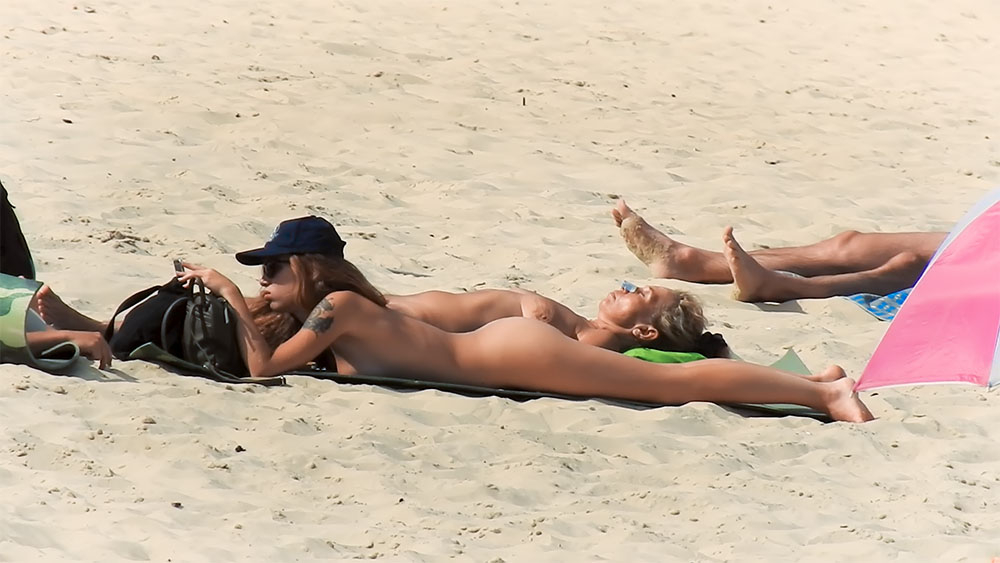 Zwei Frauen oben ohne im Sand mit blauer Kappe
